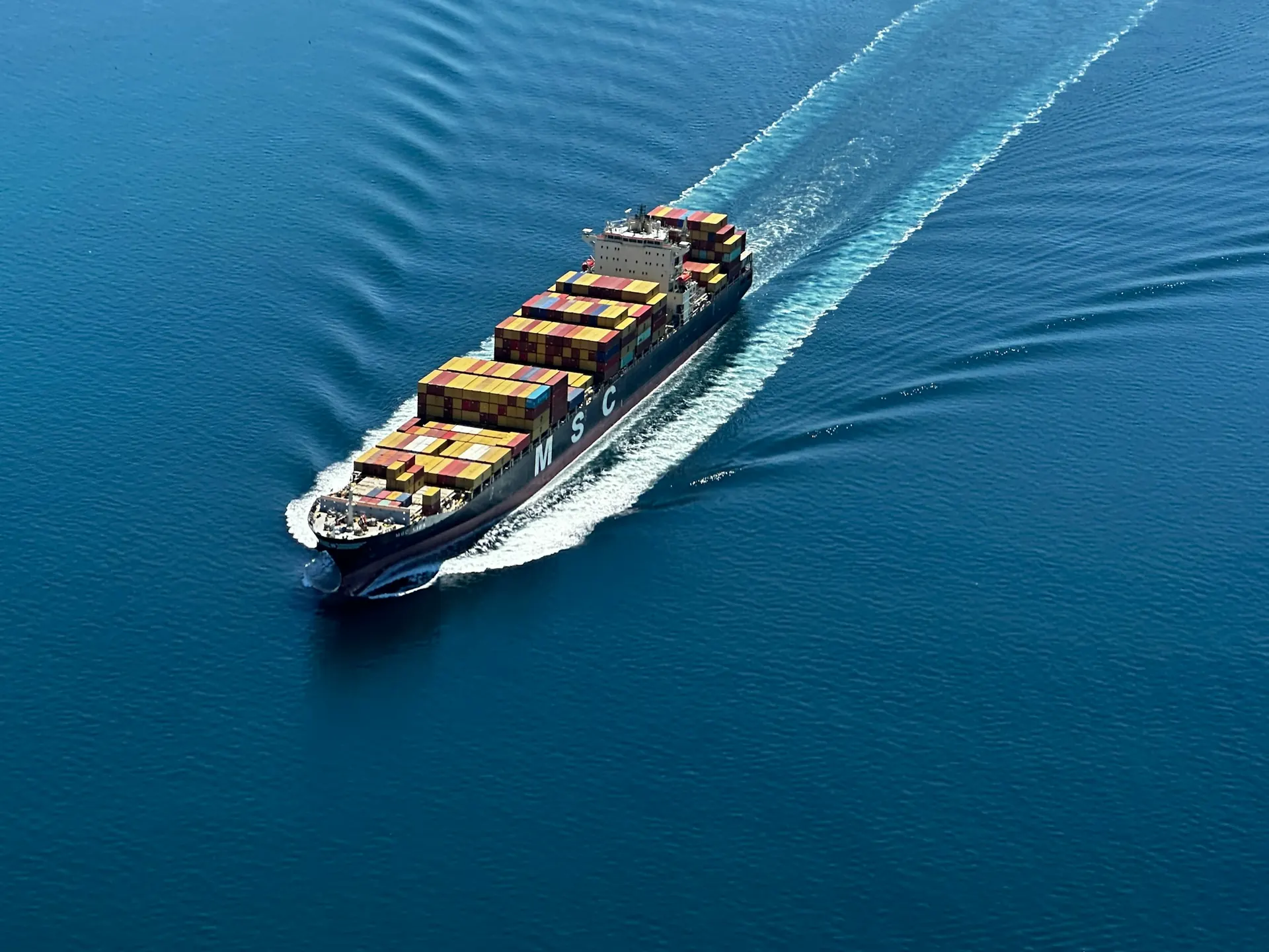 Aerial view of a container ship leaving a wake across open water