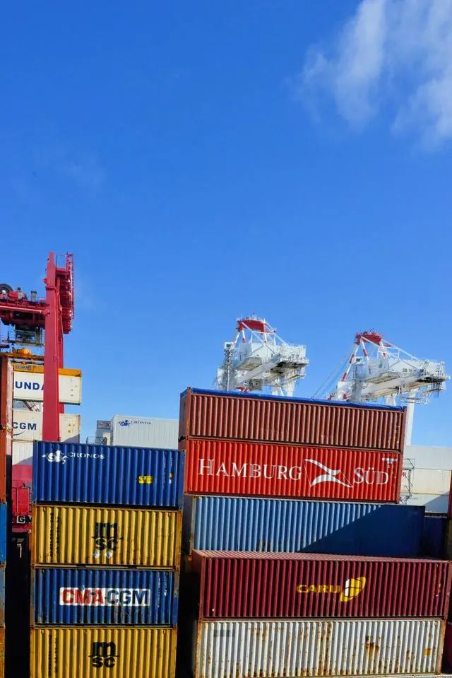 Stacked shipping containers beneath port cranes